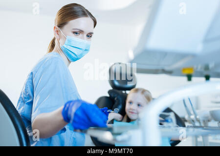 Un examen attentif. Belle femme agréable dentiste procède à une étude d'une petite fille, tenant un miroir de la bouche et en tenant une autre instrumen Banque D'Images