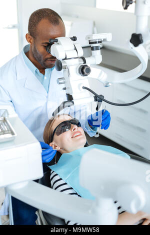 La technologie utile. Les jeunes qualifiés male dentist l'examen de la cavité orale de sa patiente et à l'aide d'un microscope à cette fin Banque D'Images