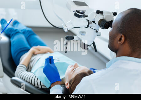 Mesure nécessaire. Qualifiés agréable contrôle dentiste dents de ses patients pour les micro-fissures à l'aide d'un microscope pendant qu'elle couchée dans le dentiste Banque D'Images