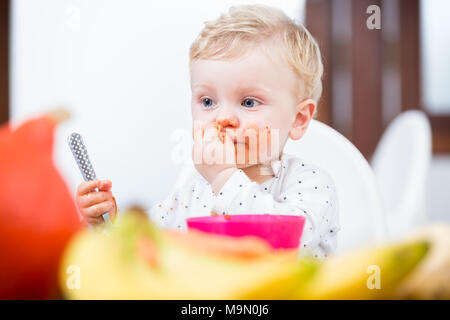 Portrait of a cute baby girl en désordre de manger avec ses mains Banque D'Images