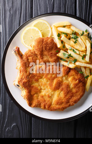 Escalope de veau poêlée Milanese avec citron et frites sur une assiette. Haut Vertical Vue de dessus Banque D'Images