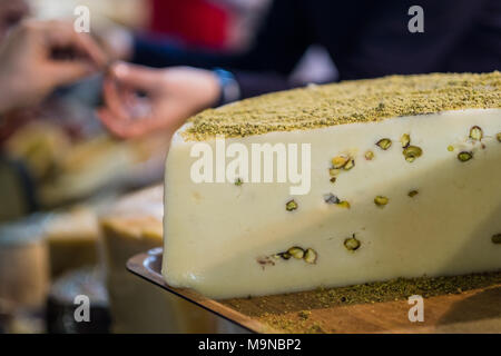 Roue de fromage délicieux avec les pistaches sur plateau en bois en épicerie fine avec le fournisseur et client à l'arrière-plan Banque D'Images