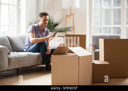 Paniers boîtes en carton avec young man sitting on sofa in living room service appelant à l'arrière-plan, effets personnels en carton en attente f Banque D'Images