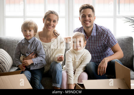 Portrait of happy couple avec adopté les petits enfants le jour du déménagement, smiling parents multinationales embrassant kids looking at camera sitting on sofa wit Banque D'Images