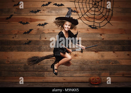 Sorcière Halloween concept - petite sorcière caucasien enfant volant sur un balai magique et bat sur spider web l'arrière-plan. Banque D'Images