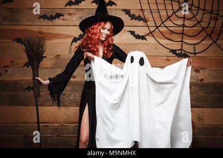 Concept Halloween Sorcière - Mère et peu de blanc faisant ghost trick or treat célébrer Halloween posant avec des citrouilles sur les chauves-souris et d'araignée sur fond de studio en bois. Banque D'Images