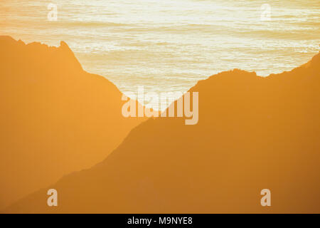 Coucher de soleil sur l'océan illumine les collines et montagnes avec des teintes et des tons de jaune, d'or, et la lumière orange à Big Sur, en Californie. Banque D'Images