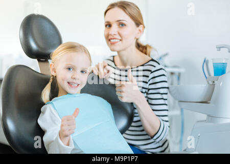 Jolie fille et sa mère showing Thumbs up bureau de dentiste Banque D'Images