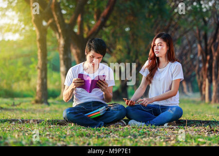 Jeune couple de lire un livre et écouter la musique avec vos écouteurs dans le parc Banque D'Images