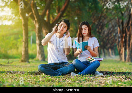 Jeune couple de lire un livre et écouter de la musique avec casque dans le parc Banque D'Images