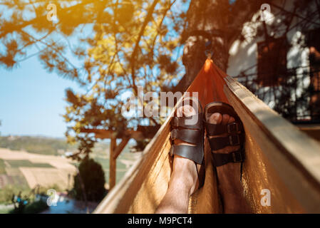 Pose de l'homme et de vous détendre dans un hamac, Close up of male détendue pieds se balançant dans le hamac dans matin d'été Banque D'Images