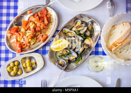 Table couverts avec les palourdes délicieux servi sur de l'argenterie, vin blanc, pain, salade de tomates et olives d'au-dessus, Portugal Banque D'Images