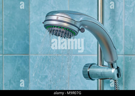 L'eau s'écoule à partir de la nouvelle tête de douche, qui est fixé sur le support dans la salle de bains privative avec des murs bleus. Banque D'Images
