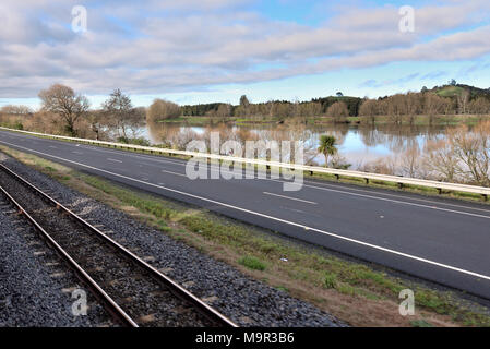 Les voies de chemin de fer qui longe une route et une rivière sous un ciel nuageux bleu Banque D'Images