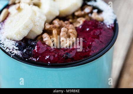 Tasse avec Smoothie bleuets congelés, les bananes, les noix, les graines de tournesol et flocons de noix de coco sur la table en bois rustique Banque D'Images