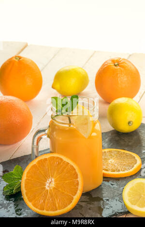 Le jus d'orange fraîchement pressé dans un pot, entouré par les oranges et les citrons en tranches une lumière d'été chaud Banque D'Images