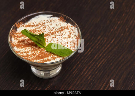 Crème Tiramisu dessert gâteau en verre avec les feuilles de menthe sur fond de bois noir Banque D'Images