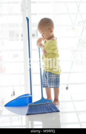 Jeune enfant faire travaux domestiques à la maison. Bébé garçon asiatique étage panoramique avec un balai. Banque D'Images