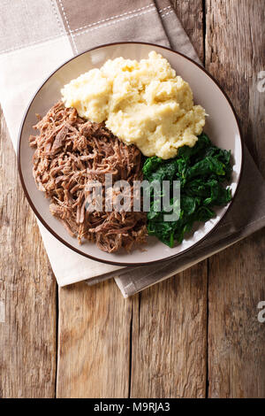 Botswana cuisine : seswaa ragoût de boeuf avec pap de porridge et de l'épinard close-up sur une plaque sur une table. Haut Vertical Vue de dessus Banque D'Images