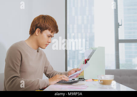 Jeune homme triste analyse des finances du foyer tout en gesticulant avec la main et à la recherche à des documents. Assis près de table avec tablette. Banque D'Images