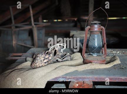 Fédération vintage articles ménagers. Stilllife. Vieille bast chaussures et une lampe au kérosène sur un morceau de sac dans un grenier poussiéreux dans la maison de campagne. Selective Banque D'Images