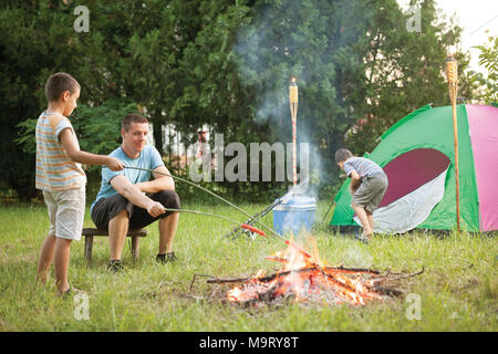 Famille sur un voyage de camping, le père et fils la cuisson des saucisses Banque D'Images