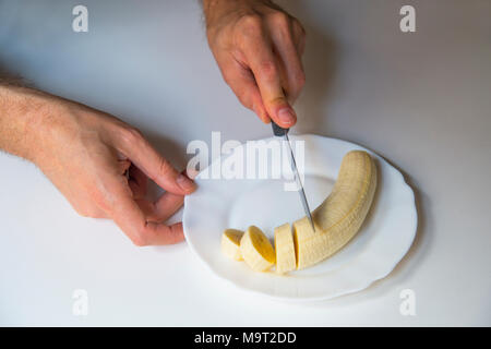 La main de l'homme la coupe une banane dans un plat. Banque D'Images