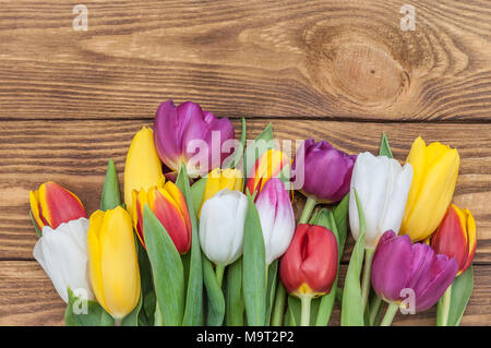 Tulipes multicolores avec une brassée au centre sur un fond de bois clair. Banque D'Images