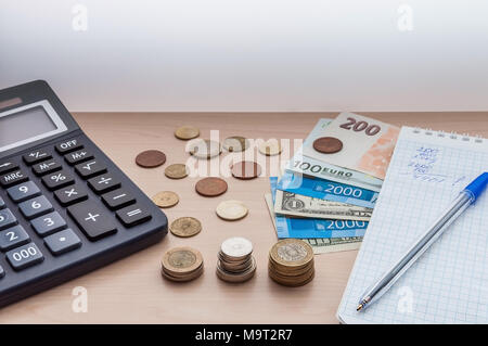 Une calculatrice, pièces de monnaie, les projets de loi et d'un ordinateur portable avec un stylo se trouvent sur la table. Banque D'Images