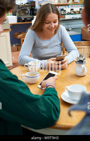 Groupe d'amis adolescents réunion dans un café et l'utilisation de téléphones mobiles Banque D'Images