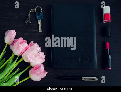 Femme est rose et noir accessoires sur fond en bois foncé avec bouquet de tulipes. Business Woman concept. Le modèle de mode sur les travaux. Mise à plat. Banque D'Images