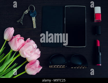 Femme est rose et noir accessoires sur fond en bois sombre et d'un téléphone mobile avec écran vide. Bouquet de tulipes roses. Business Woman concept. Fashi Banque D'Images