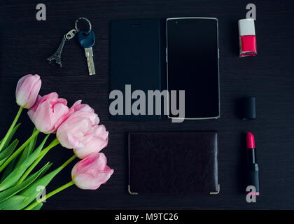 Femme est rose et noir accessoires sur fond en bois sombre et d'un téléphone mobile avec écran vide. Bouquet de tulipes roses. Business Woman concept. Fashi Banque D'Images