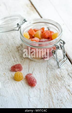 Gummy vitamines dans le bocal en verre blanc sur fond de bois. Bonbons multivitaminés en forme de différentes sortes de fruits. Supplément Nutrition concept. Banque D'Images