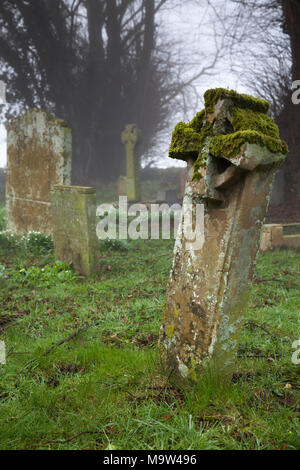 Un matin brumeux parmi les pierres tombales dans un cimetière, l'église All Saints, Holdenby, Northamptonshire, Angleterre. Banque D'Images