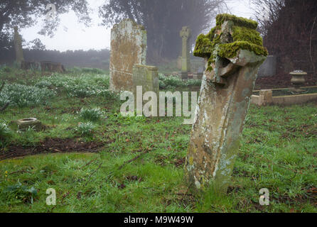 Un matin brumeux parmi les pierres tombales dans un cimetière, l'église All Saints, Holdenby, Northamptonshire, Angleterre. Banque D'Images