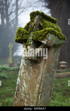 Un matin brumeux parmi les pierres tombales dans un cimetière, l'église All Saints, Holdenby, Northamptonshire, Angleterre. Banque D'Images