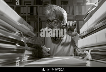 Chercheur Senior à l'aide d'une loupe et d'écriture, il est entouré par des piles de paperasse Banque D'Images