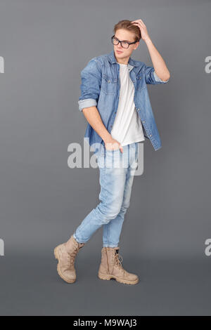 Jeune homme en jeans jacket studio isolé sur cheveux toucher gray Banque D'Images