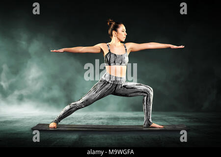 Monter athletic jeune femme démontrant le guerrier 2 poser dans le yoga se précipitant vers l'étirement avec bras tendus tout droit Banque D'Images