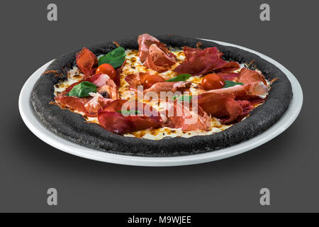 Pizza italienne avec tomates cerises, prosciutto et basilic isolé sur fond sombre Banque D'Images