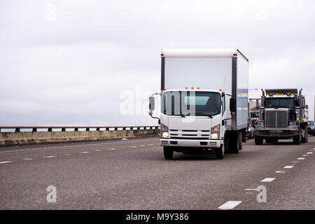 Petit parc de camions semi-remorque avec fort et gros camion semi classique de la flotte de camions fonctionnant sur une large autoroute avec circulation à gauche derrière Banque D'Images