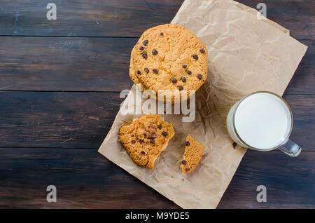 Les cookies avec pastilles de chocolat sur du papier craft et un verre de lait sur fond de bois foncé. copy space Banque D'Images