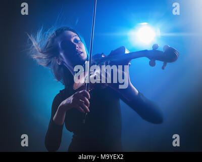 Belle jeune femme à jouer du violon avec le vol des cheveux sur un fond bleu. Studio shot Banque D'Images