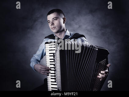 Musicien à jouer de l'accordéon sur un fond noir. Le brouillard à l'arrière-plan. Studio shot Banque D'Images