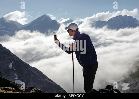 Hipster homme tire une vidéo d'un paysage de montagne avec des nuages sur un téléphone mobile, alors que l'article de fond contre les hauts sommets. L'homme est tak Banque D'Images