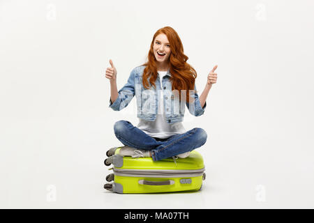 Voyager et le style de concept. Les jeunes enthousiastes caucasian woman sitting on l'assurance valise showing thumb up. Isolé sur blanc. Prêt pour les vacances. Banque D'Images