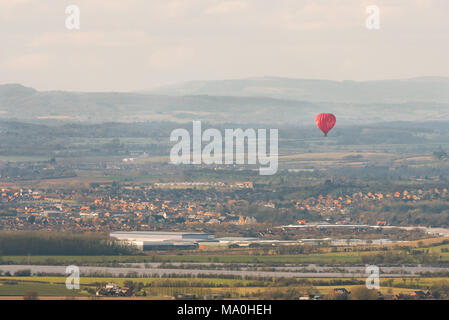 Un seul les red hot air ballon vole flottant au-dessus de maisons d'une petite ville de la campagne environnante. Banque D'Images