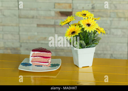 Gâteau aux fraises sur le plat blanc et jaune fleurs artificielles dans un vase blanc repose sur table en bois jaune Banque D'Images