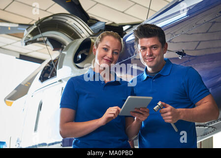 Portrait d'Aero Ingénieur et apprenti travaillant sur hélicoptère dans Hangar Looking At Digital Tablet Banque D'Images